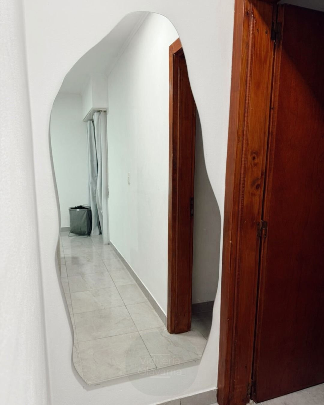 Espejo de pared con reflejo distorsionado en un pasillo estrecho junto a unas puertas de madera.