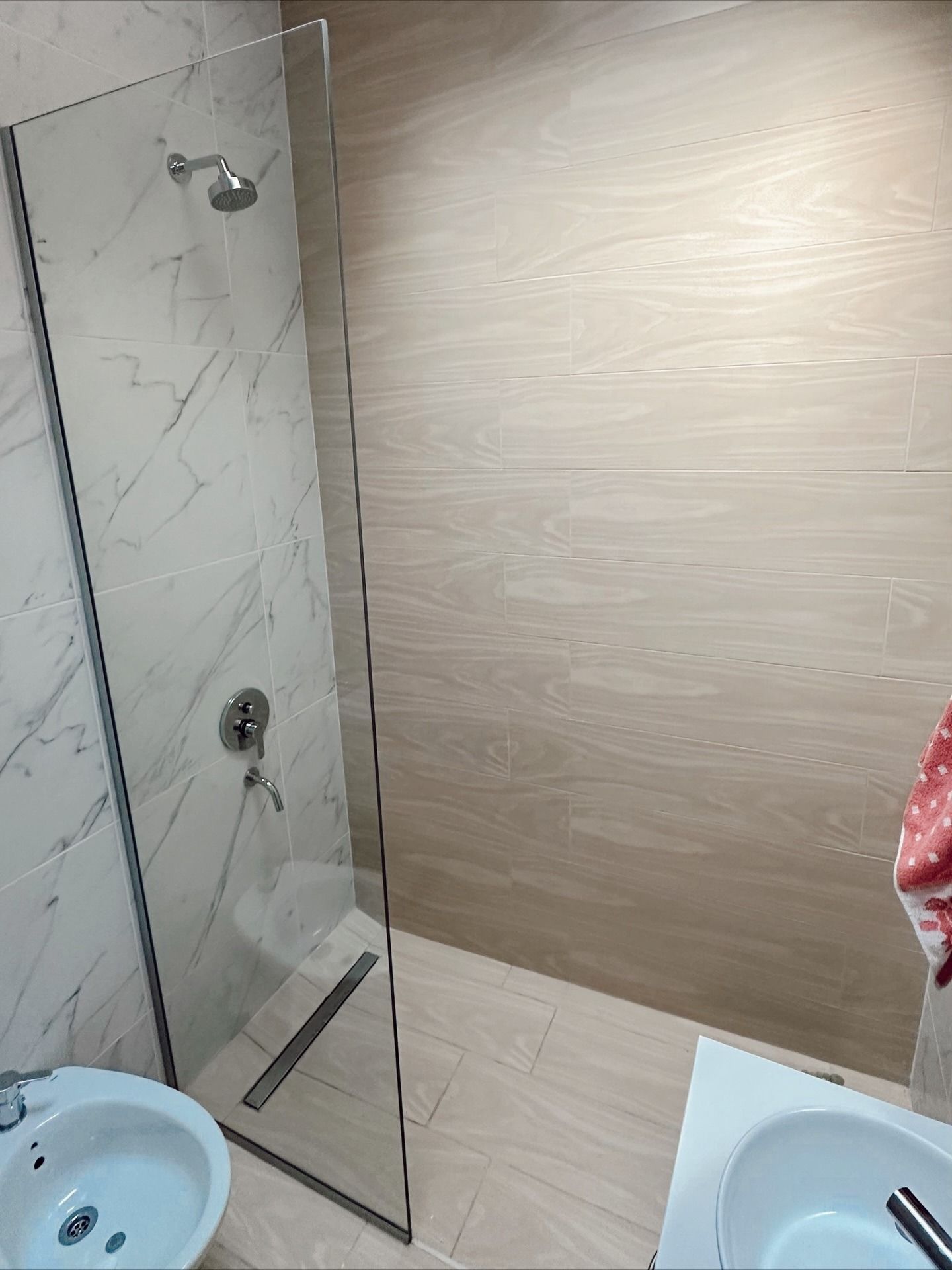 Baño pequeño con ducha de cristal, paredes alicatadas en color beige y un lavabo blanco en primer plano.
