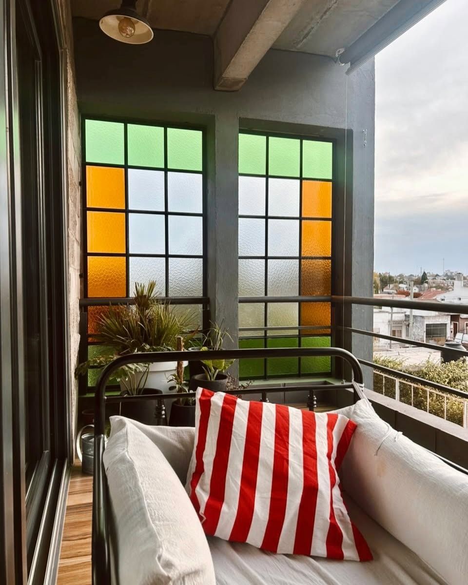 Asientos en el balcón con una silla blanca y un cojín de rayas rojas junto a vidrieras con vistas a la ciudad.
