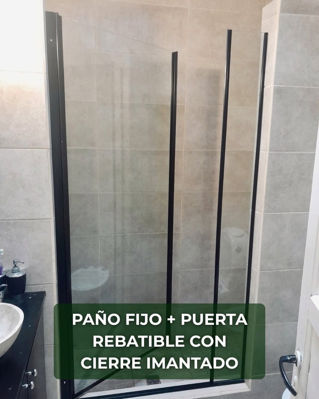 Baño con mampara fija y puerta abatible con cierre de manto, en vidrio oscuro y perfil negro.