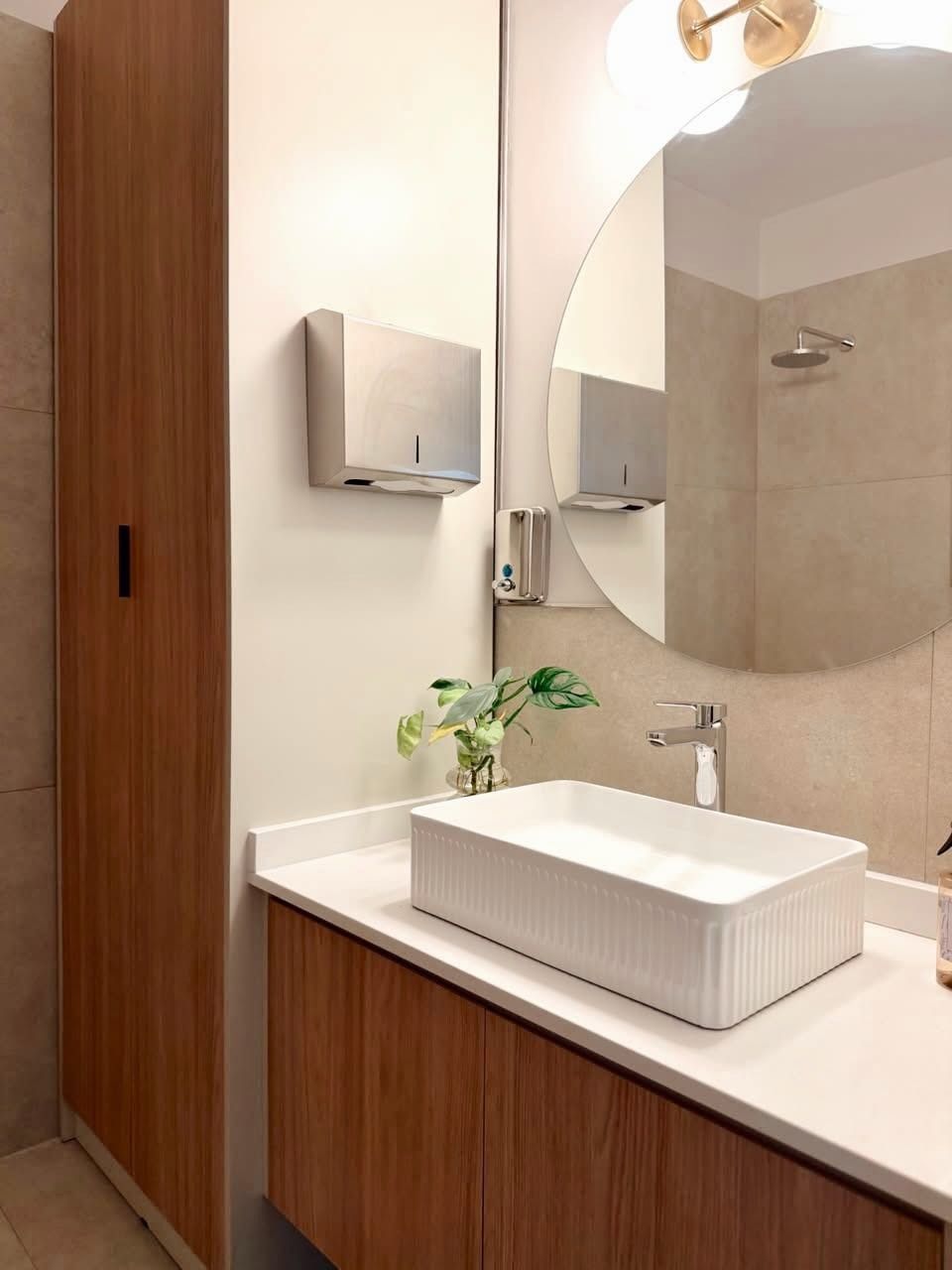 Tocador de baño moderno con lavabo sobre encimera, espejo redondo y armarios de madera.