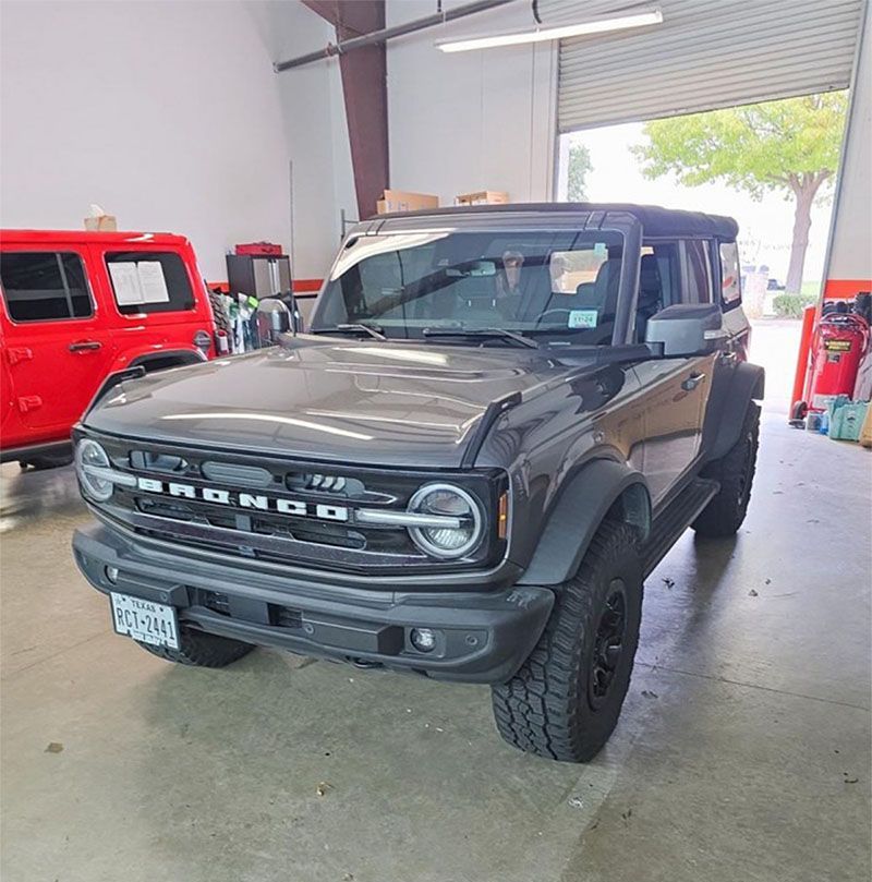 A black ford bronco is parked in a garage next to a red jeep.