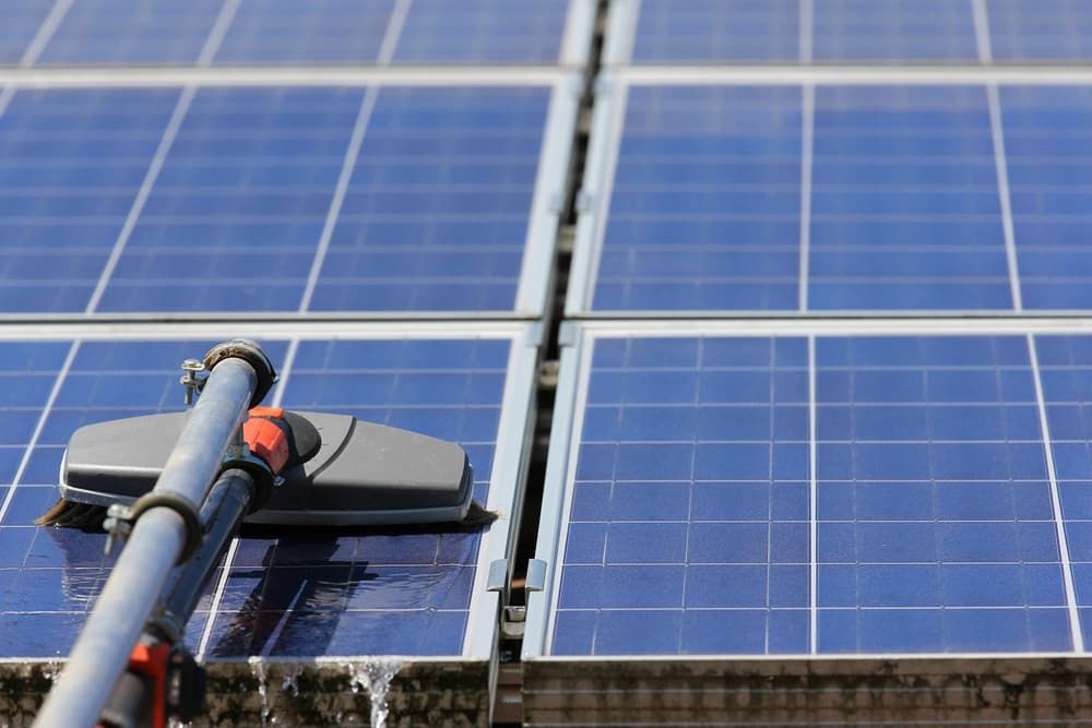 A Person is Cleaning a Solar Panel With a Broom — TK Guttercleaning in Lake Munmorah, NSW