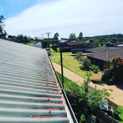 Rooftop view of a quiet suburban street with houses, trees, and a paved path under a bright sky
