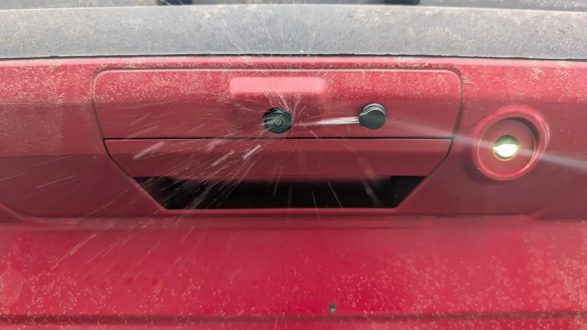 ClearVU nozzle spraying washer fluid onto a dusty red pickup's backup camera