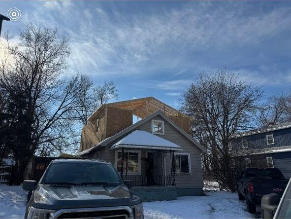 A car is parked in front of a house that is being built.