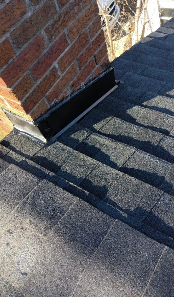 A brick chimney is sitting on top of a roof next to a brick wall.