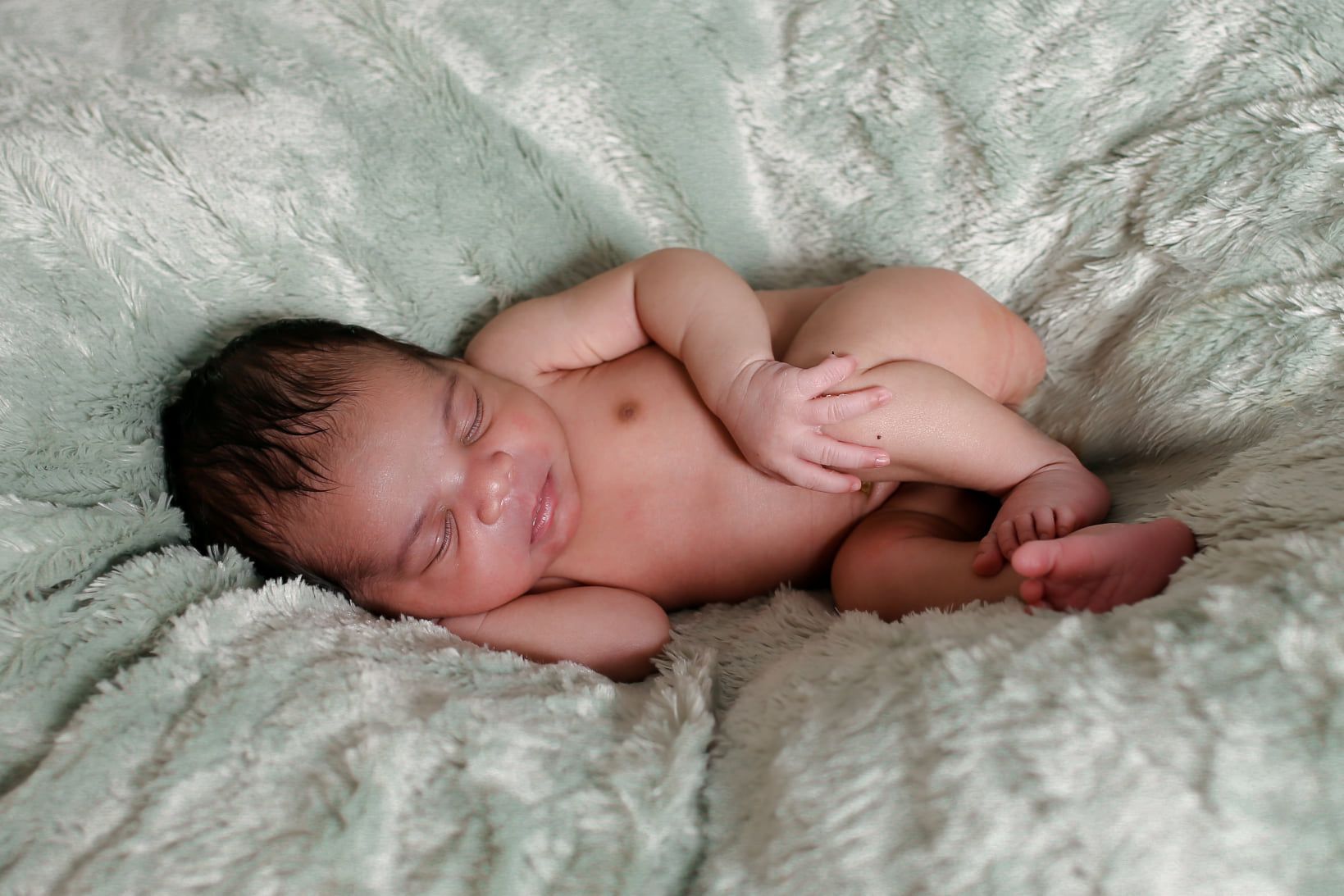 Sleeping newborn curled on a fluffy white blanket