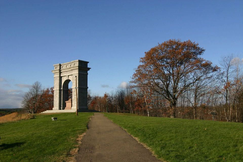 Stone monument arch beside a path in a grassy field under a blue sky