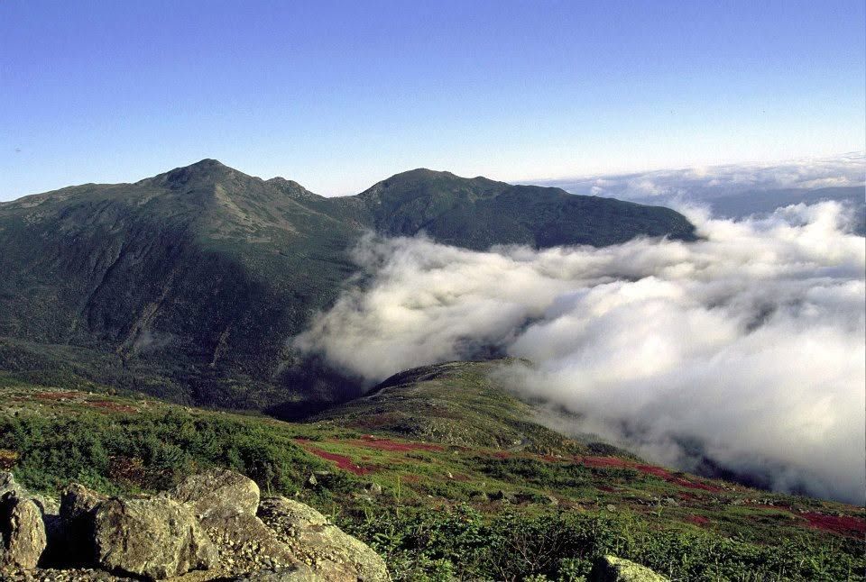 Mountain landscape with green slopes and clouds rolling over the valley under a blue sky