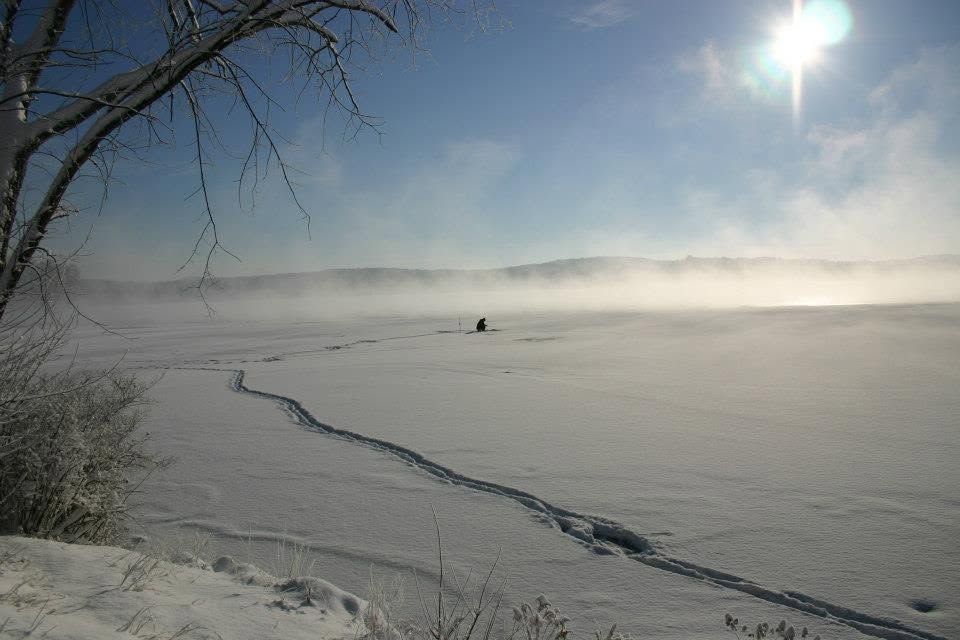 Snowy frozen lake under bright sun, with mist drifting over the icy surface.