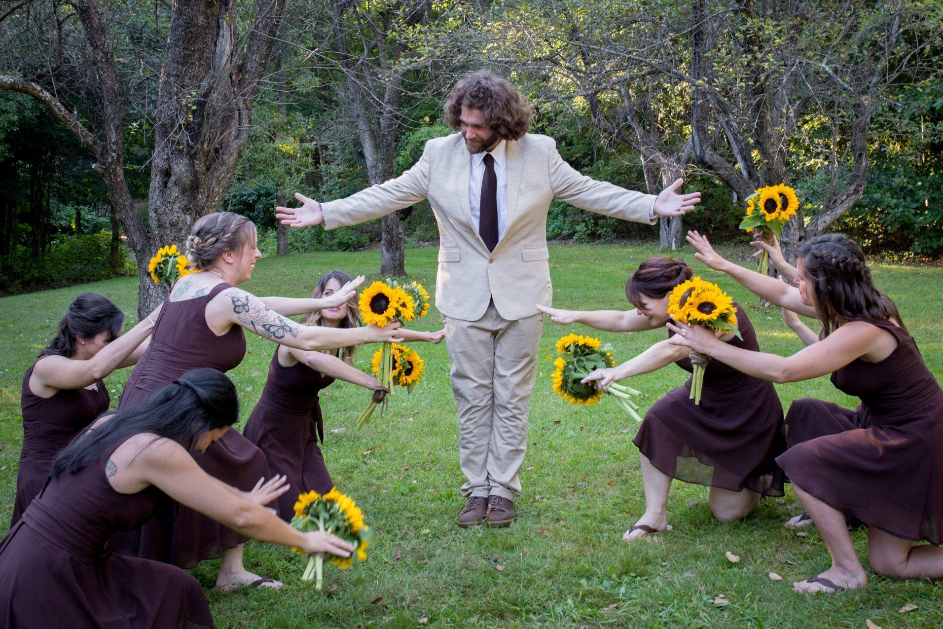 Group in a garden surrounds a person in beige, extending sunflowers toward them