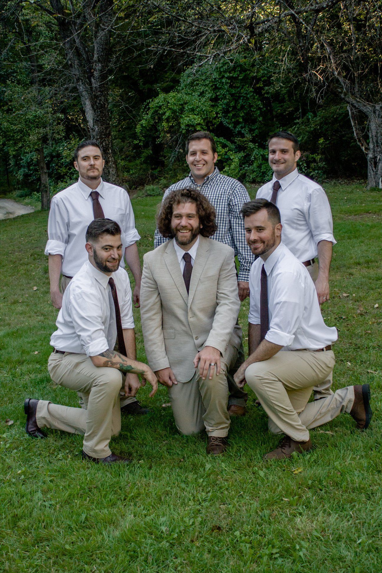 Five people posing outdoors on grass, four standing behind and two kneeling in front, dressed in formal attire