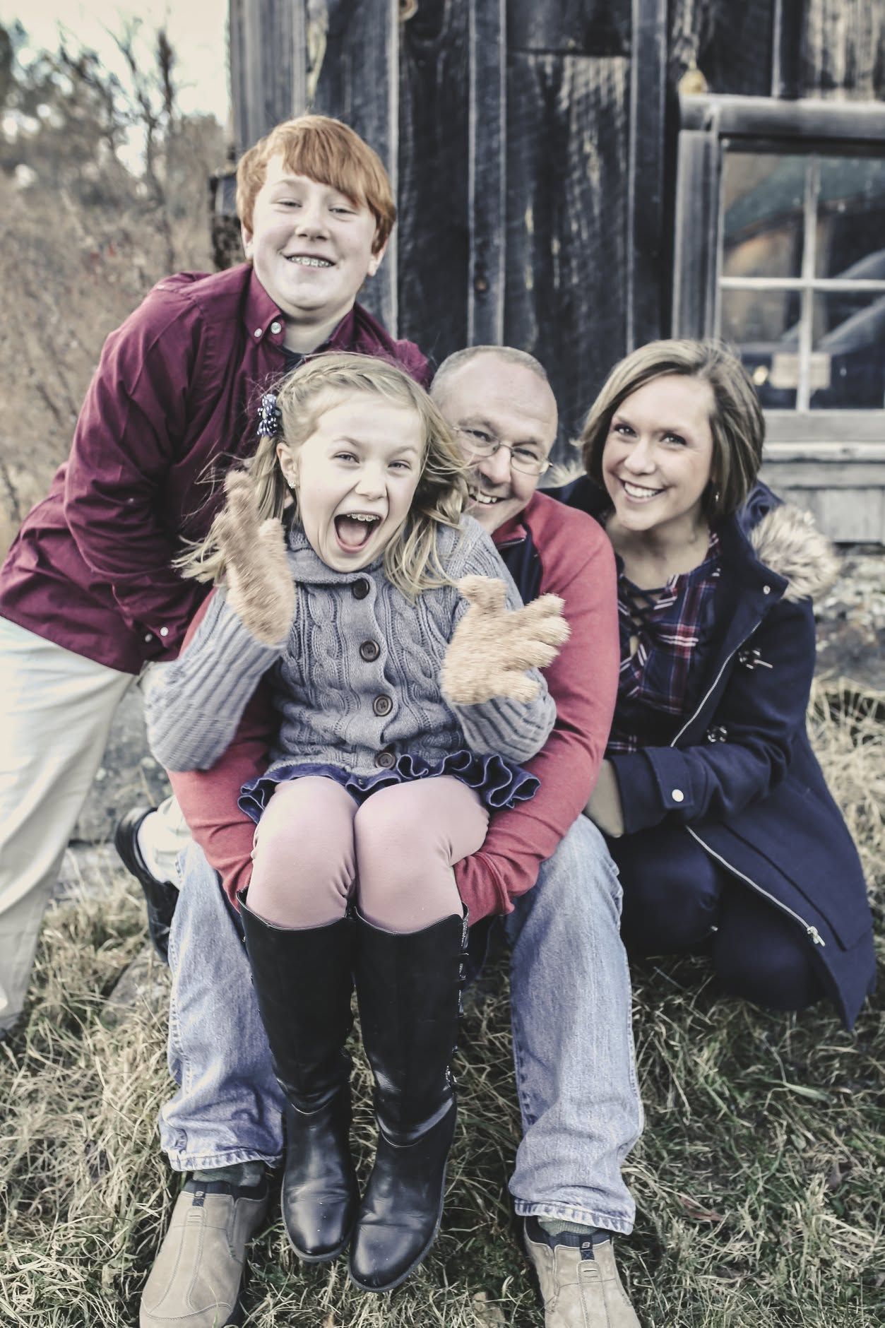 Four people smiling and posing together outdoors in front of a rustic building