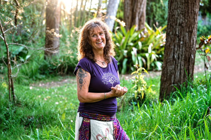 Tina, Spinal Flow practitioner at Akiki Spinal Flow, Sunshine Coast QLD. Smiling woman in a pink top standing outdoors in a garden with greenery behind her