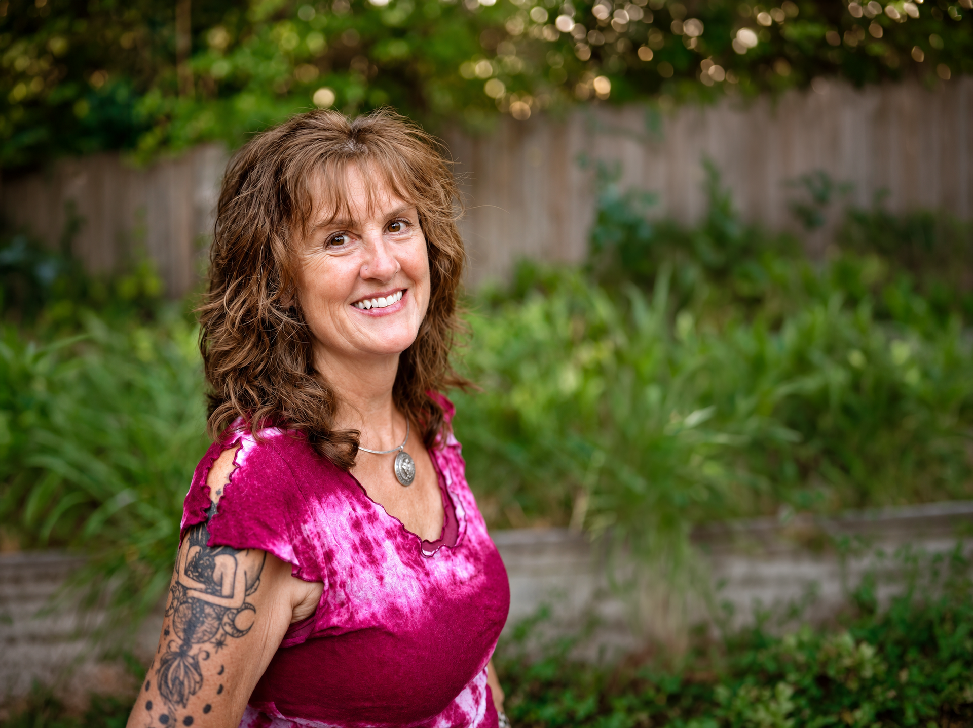 Tina, Spinal Flow practitioner at Akiki Spinal Flow, Sunshine Coast QLD. Woman in a pink top smiling outdoors in a garden setting