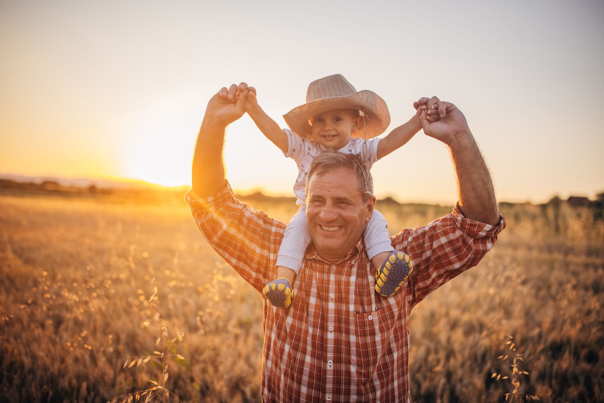 Grandfather holding child on shoulders in a field, symbolizing family-focused retirement planning and financial security