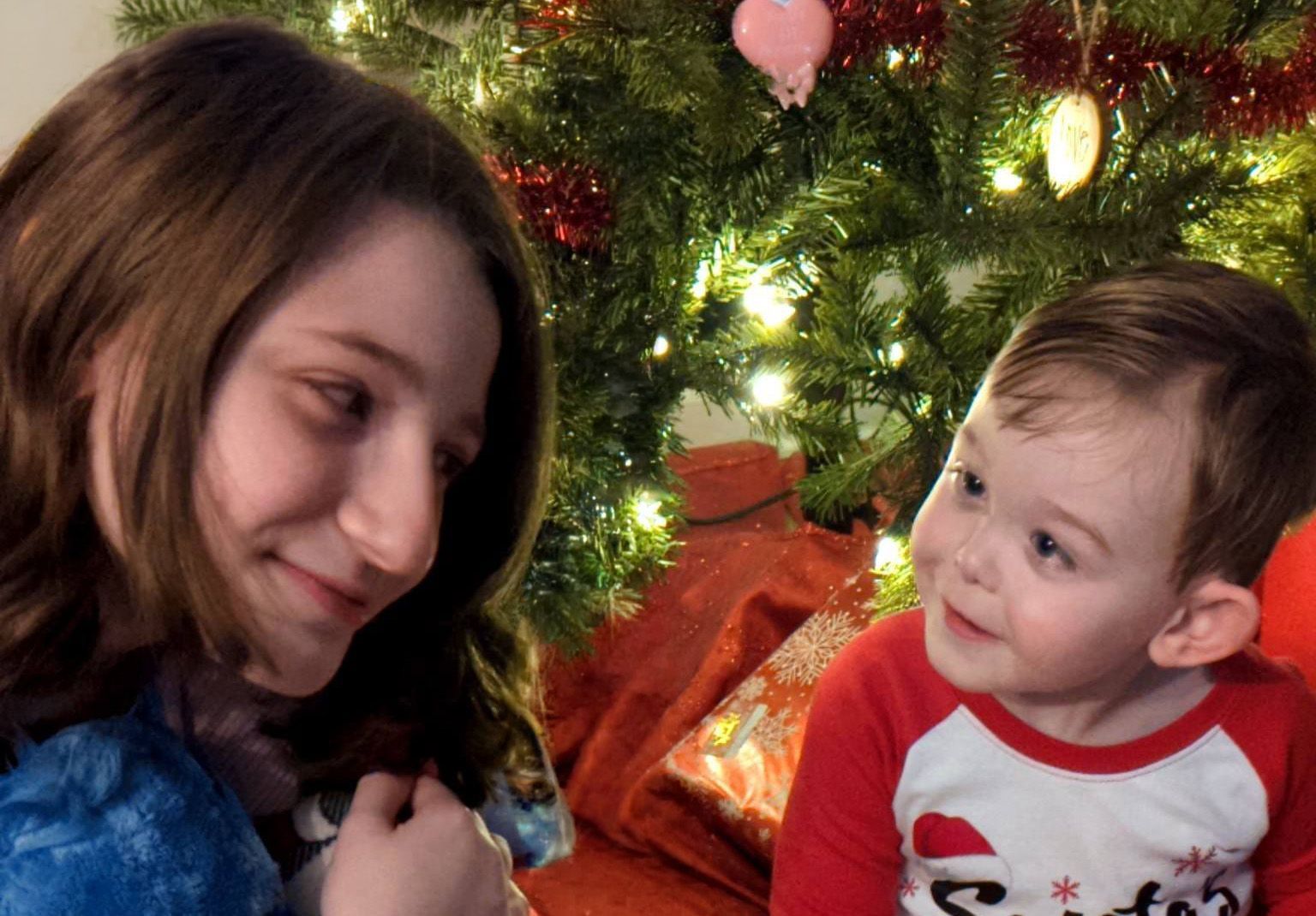 Woman and baby smiling at each other beside a decorated Christmas tree