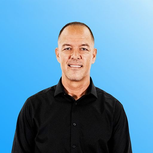 Man in a gray suit and black tie standing against a blue background