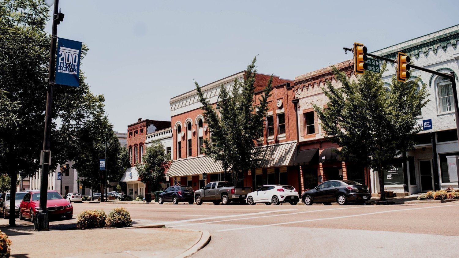 Downtown street with brick storefronts, parked cars, and a traffic light at an intersection