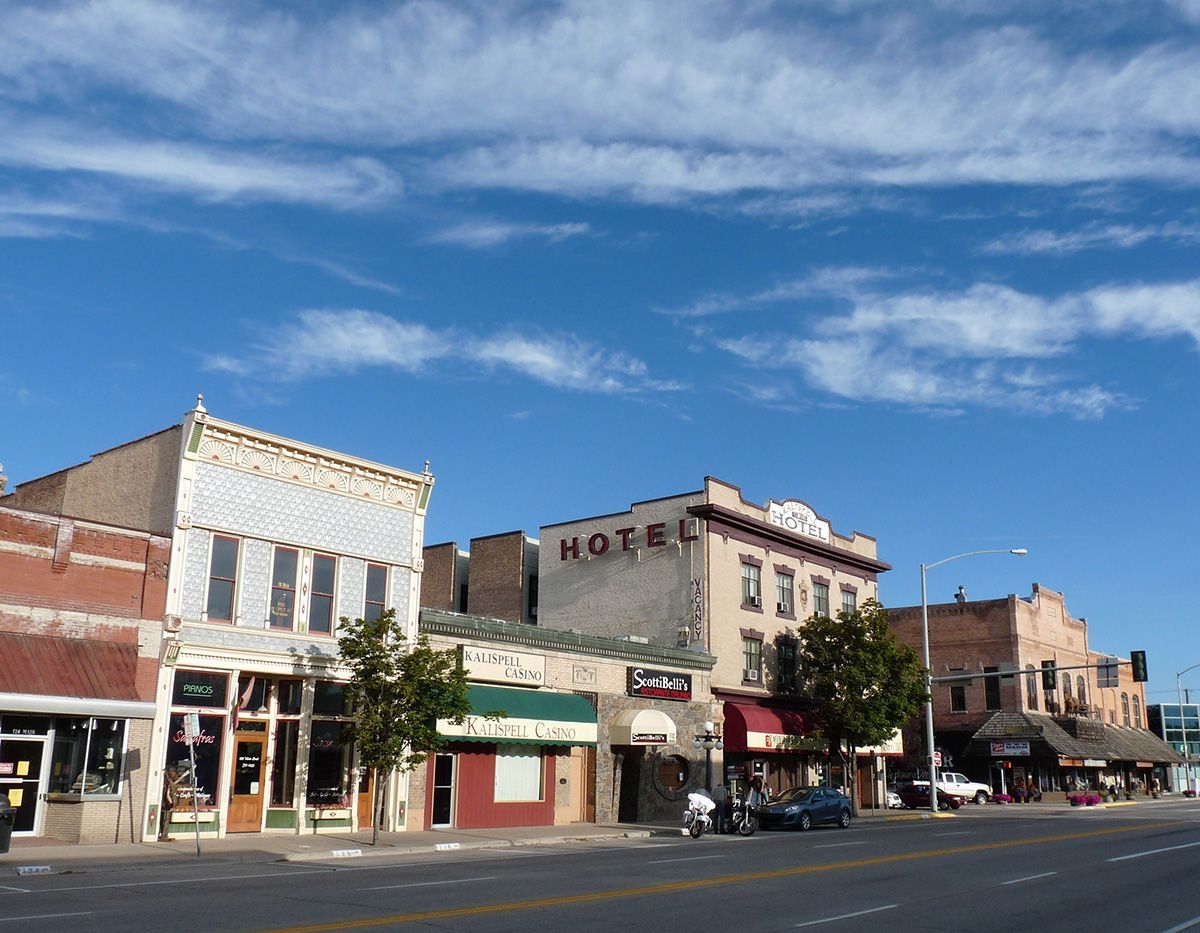 Small downtown street with historic storefronts, brick buildings, and a blue sky with wispy clouds.