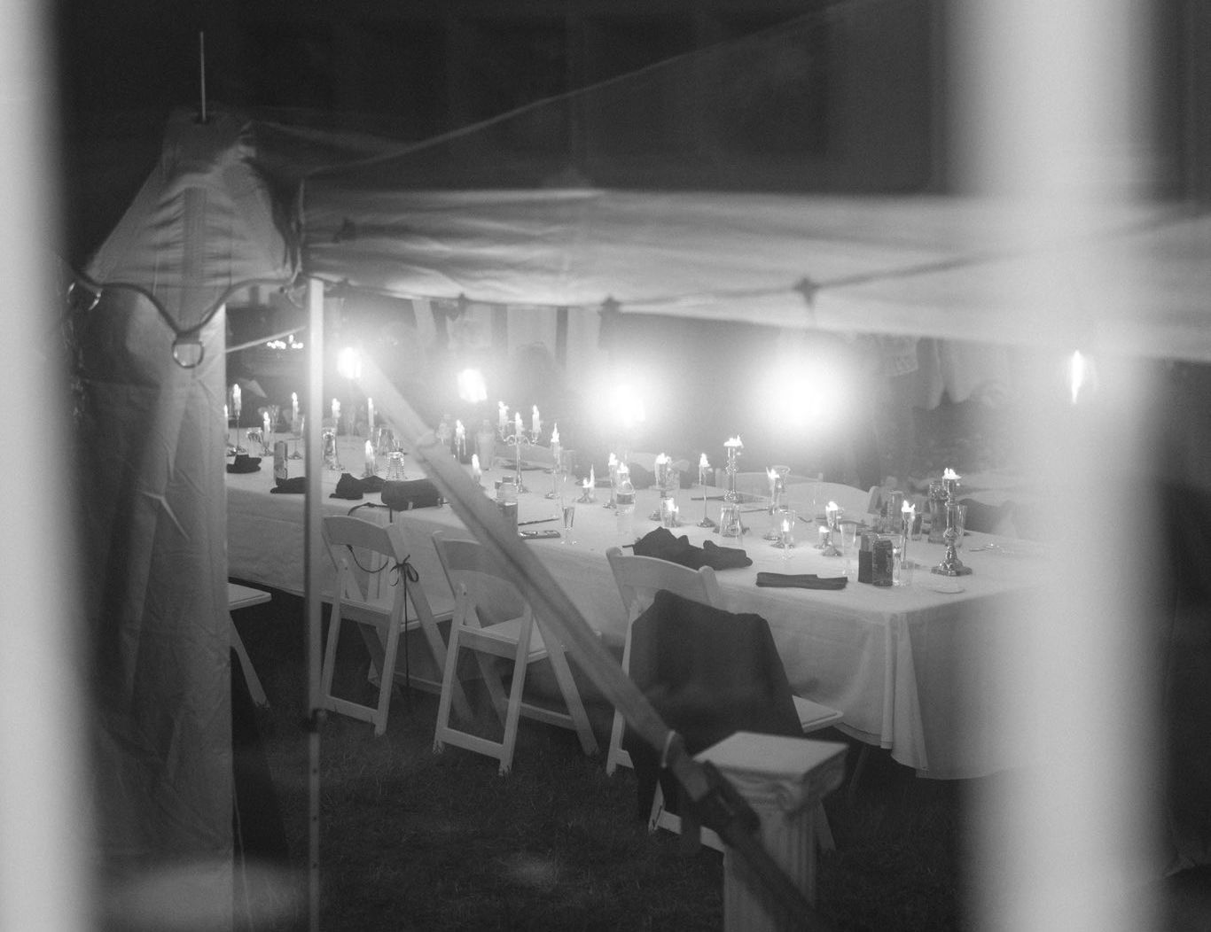 Black-and-white outdoor dining area with rows of tables and chairs under a large canopy at night