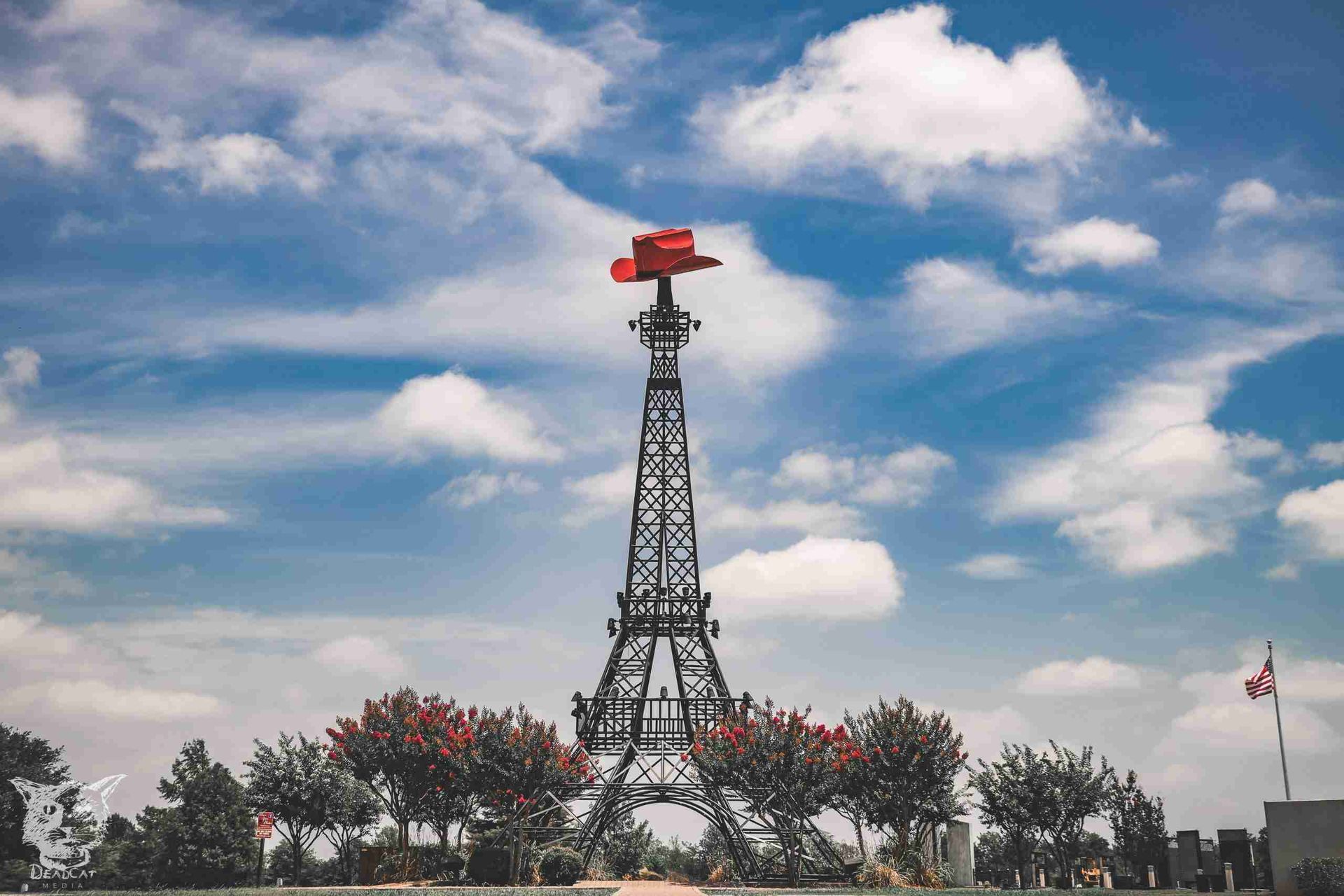 Tall metal tower with a red windmill atop it against a cloudy blue sky, with trees below.