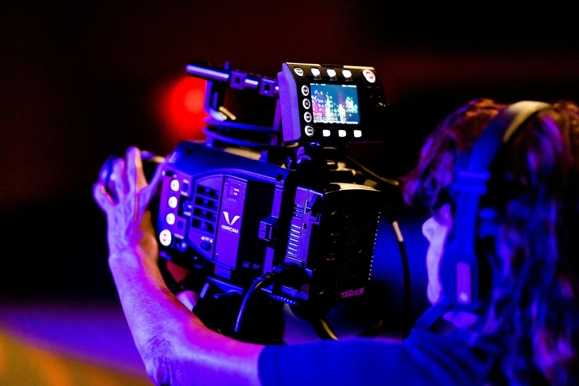 Person operating a professional video camera in dramatic red and blue lighting