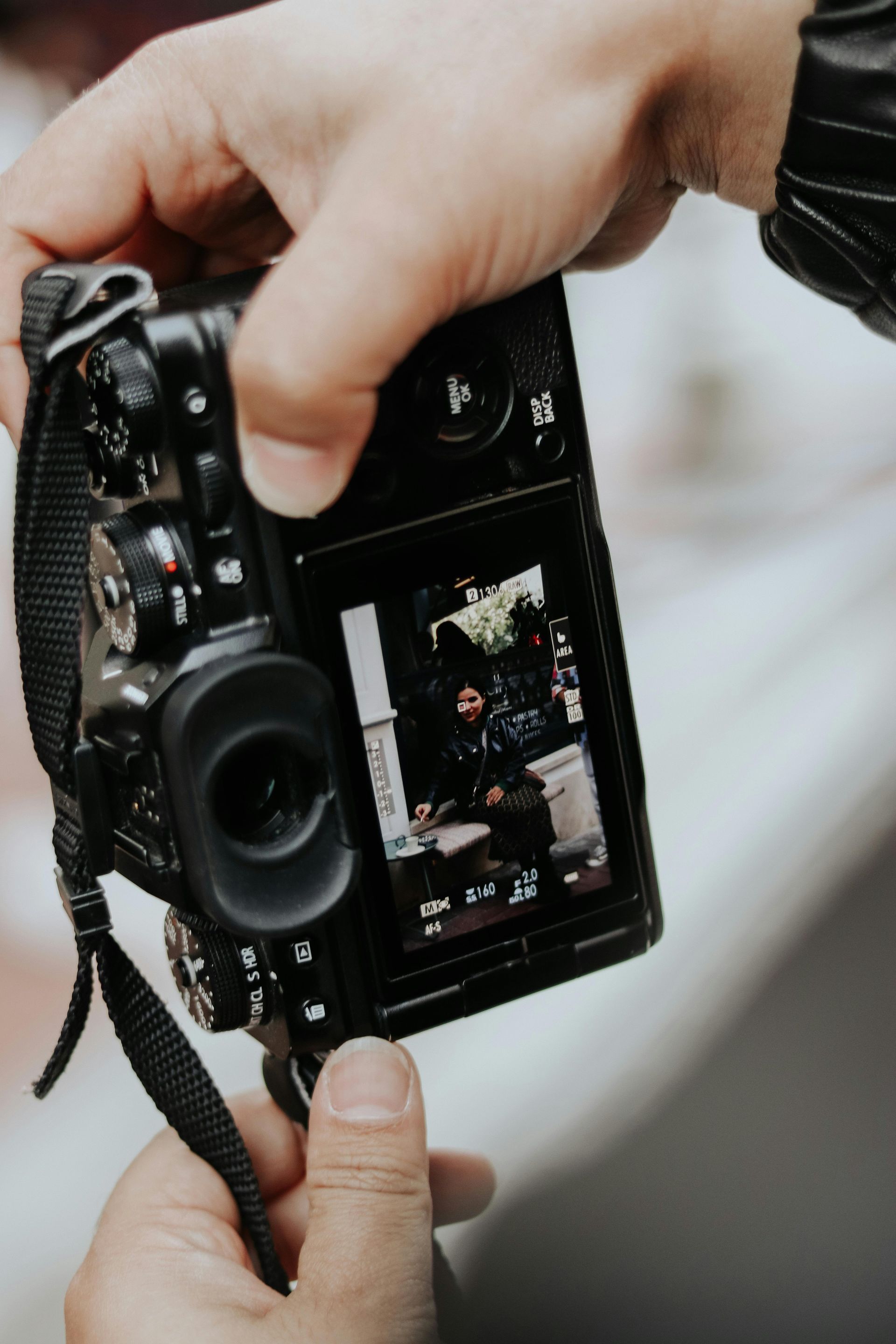 Hands holding a black camera, viewed from behind, with the screen showing a photo being captured.