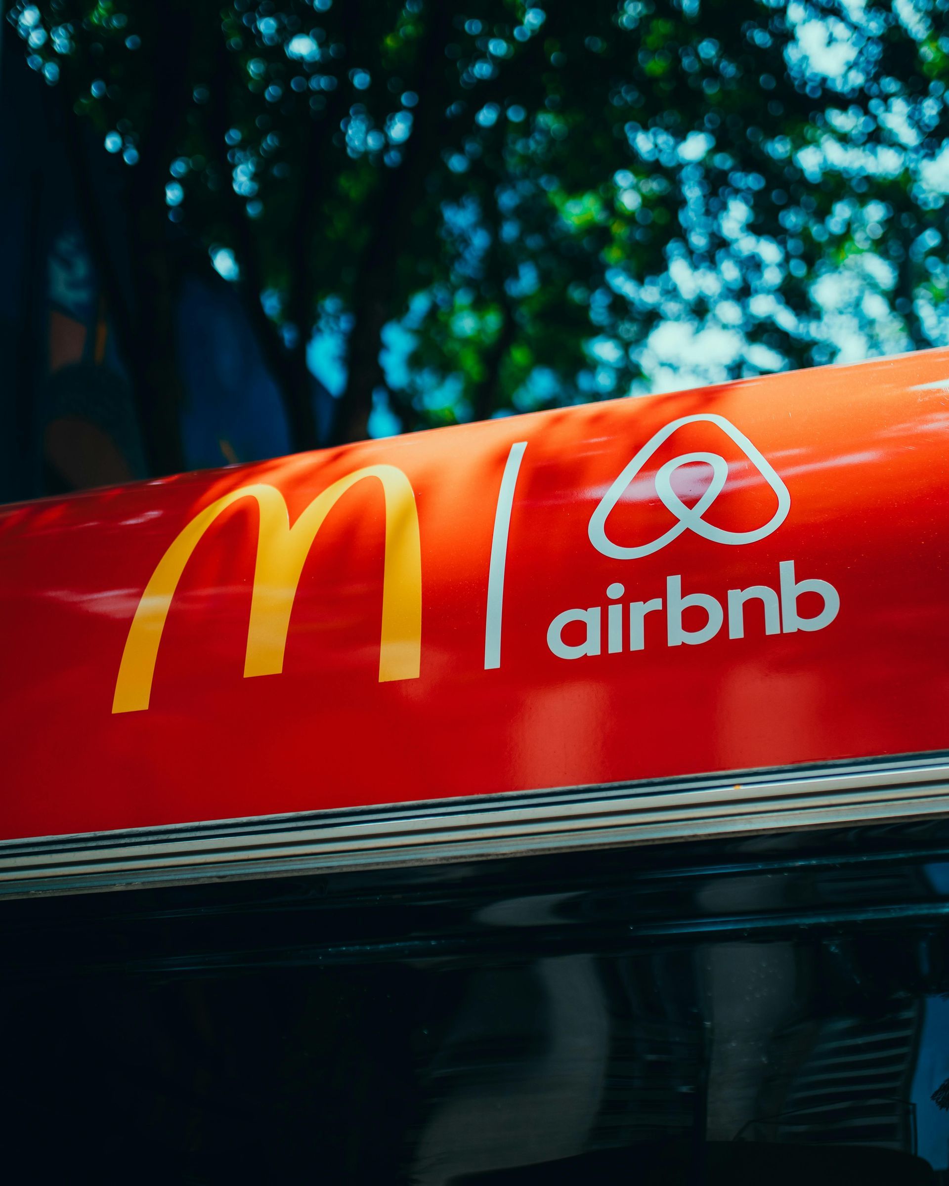 Red sign with McDonald’s and Airbnb logos side by side against a blurred outdoor background