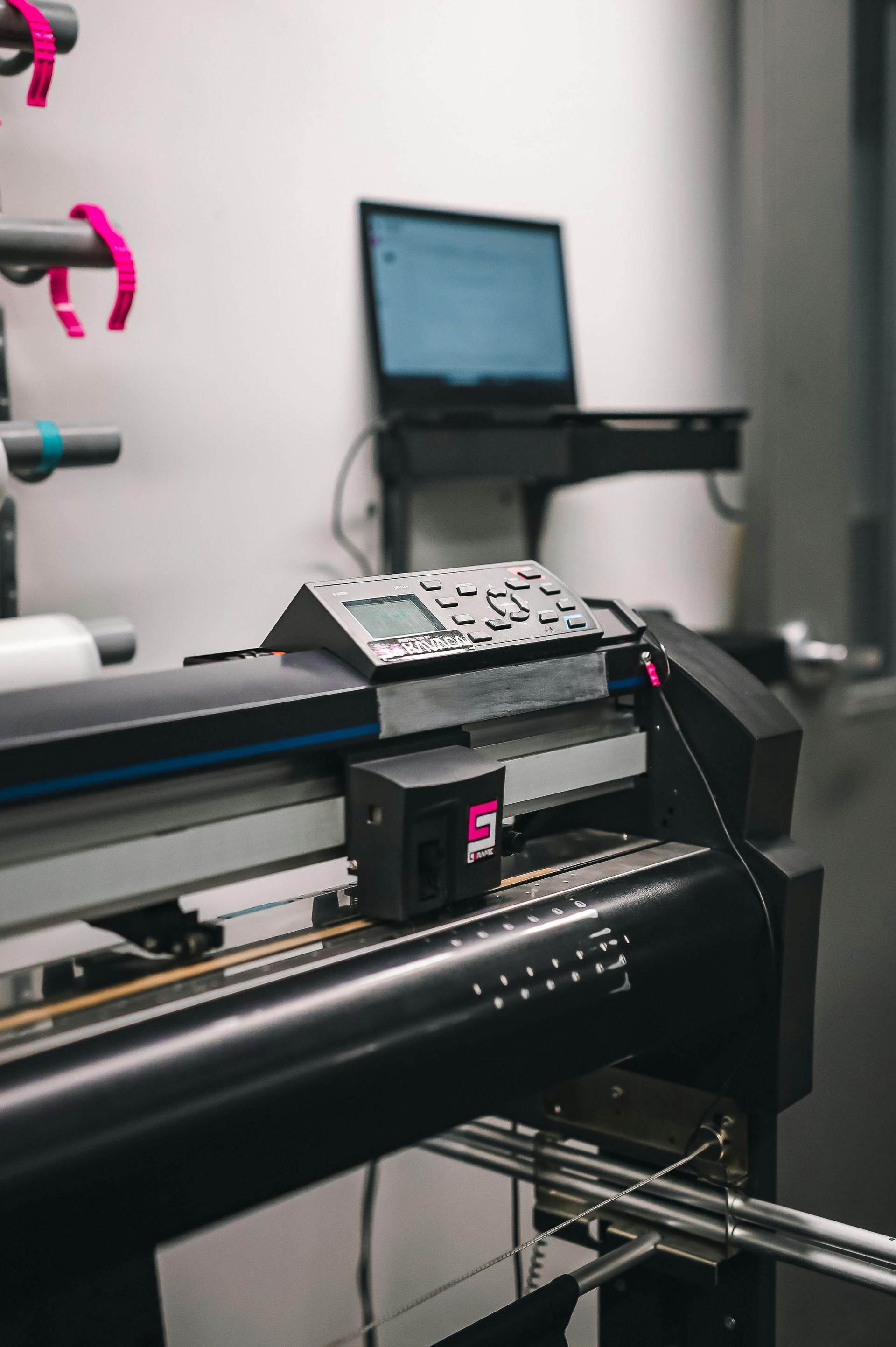 Industrial printer printing a sheet in a workshop, with a laptop in the background.