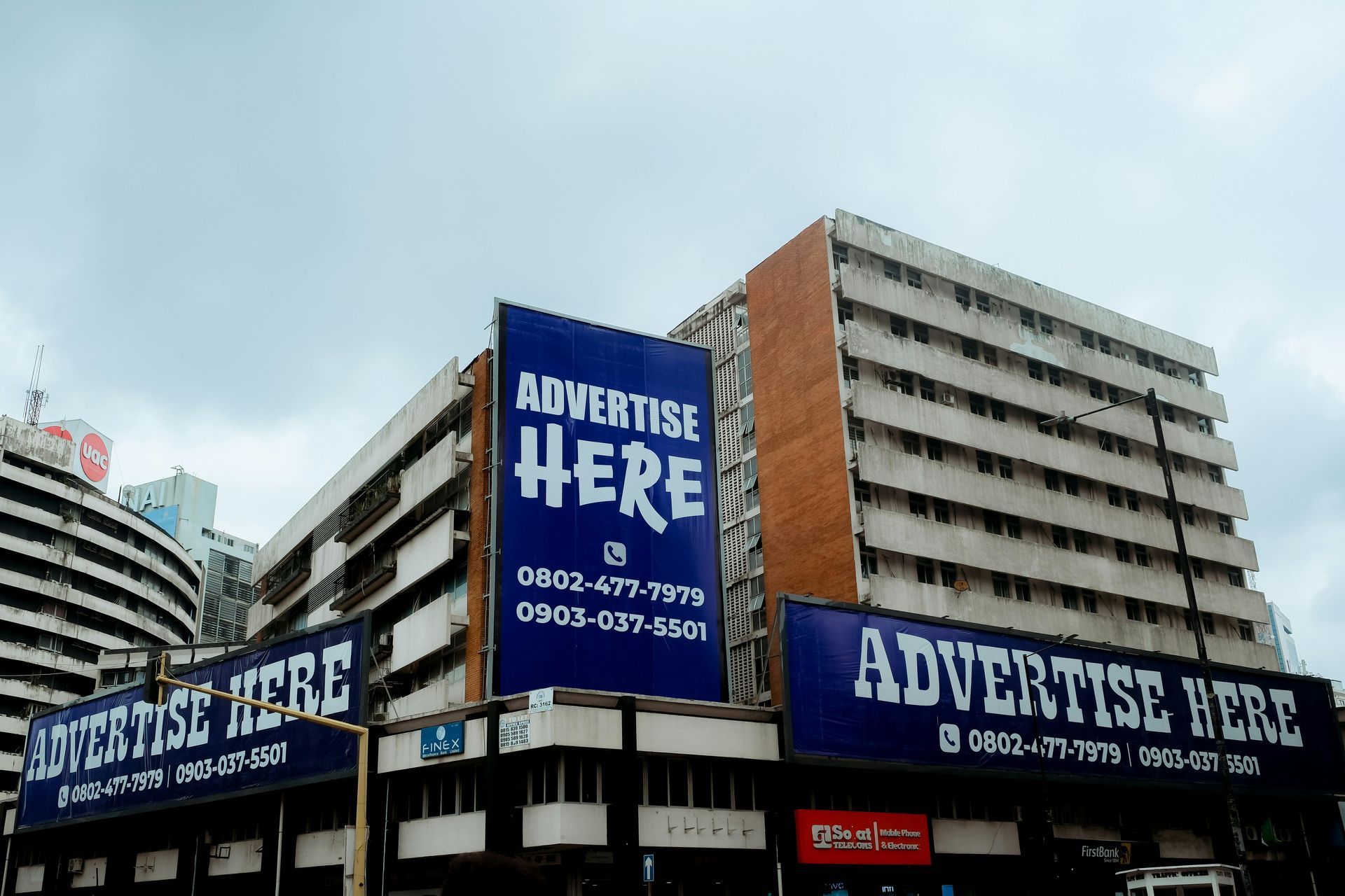 Large building covered with blue “ADVERTISE HERE” billboards against a cloudy sky.