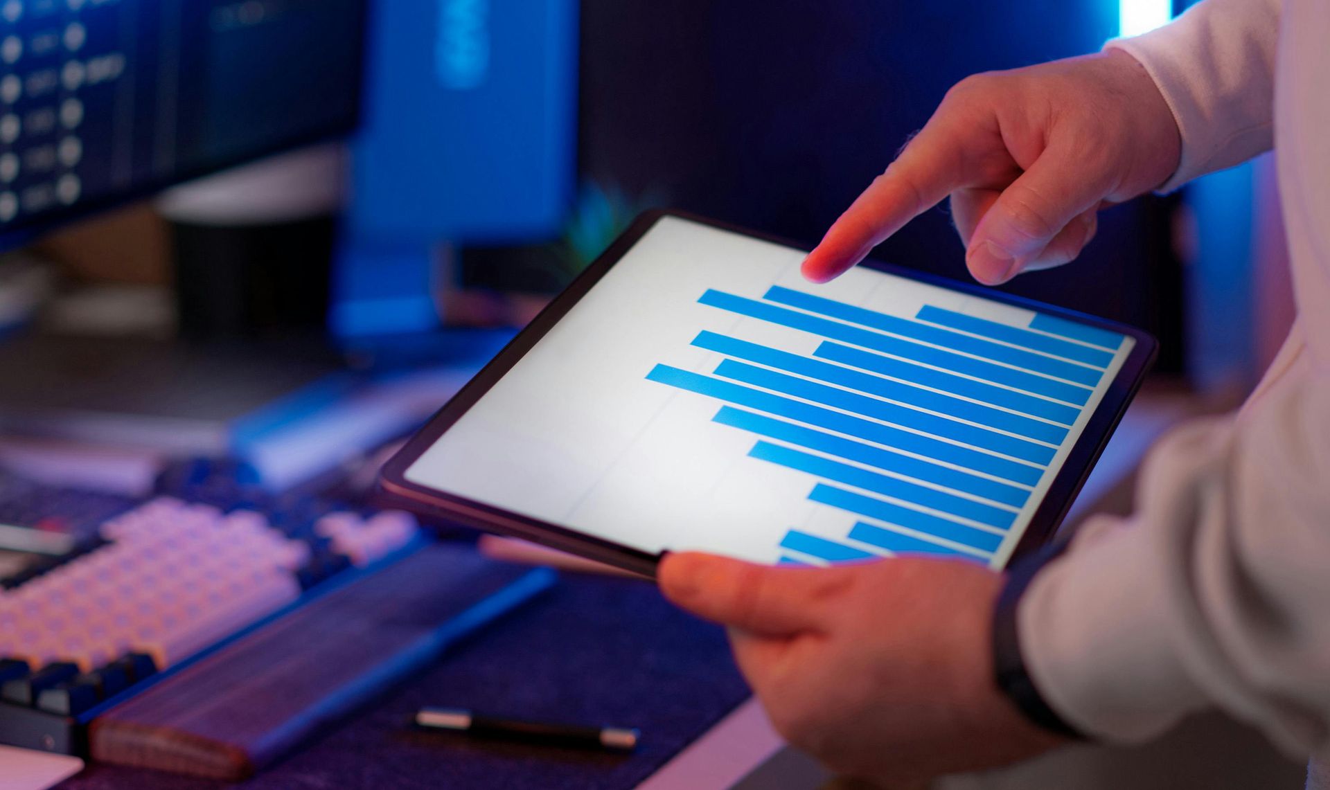 Hands holding a tablet with blue bar charts in a dim office setting