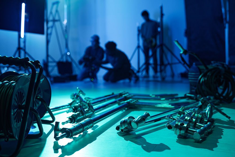 Metal camera rig parts on a studio floor with blue lighting and blurred crew in the background
