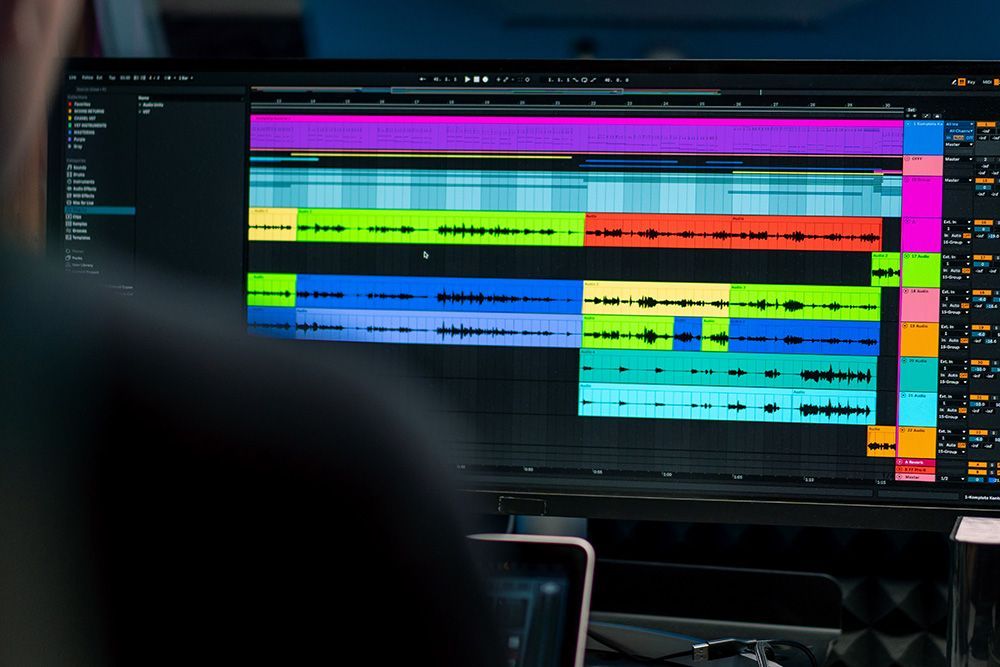 Audio editing software on a monitor with colorful tracks and waveforms, viewed over a desk