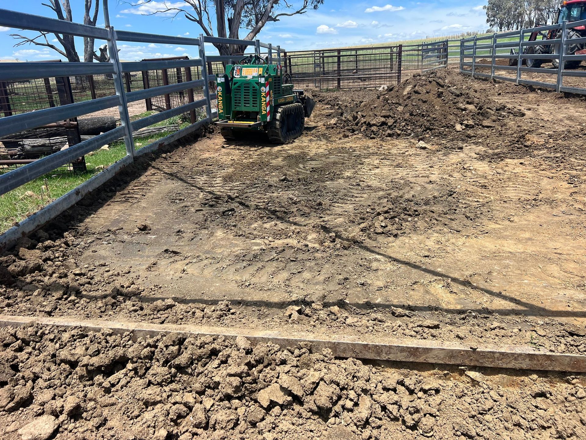 A green tractor is driving down a dirt road next to a fence.