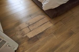 An area of wooden flooring near a bed shows significant color fading, likely from sun exposure.