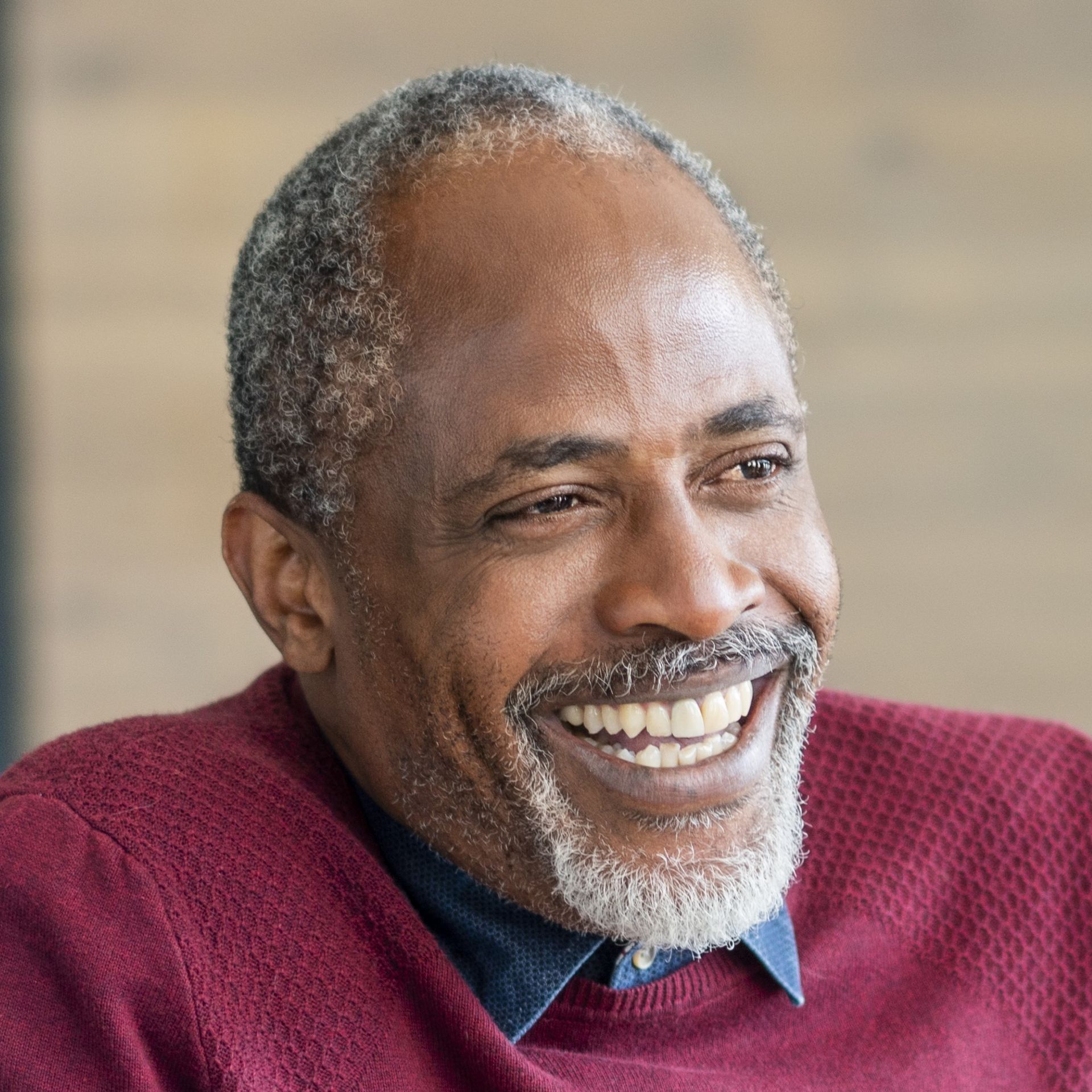 A man with a beard is wearing a red sweater and smiling.