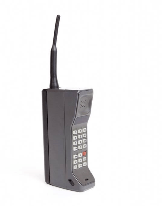 An old brick-style cell phone from the 1980's with a long antenna on a white background.