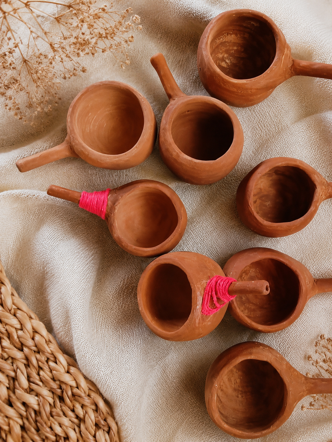 Tazas pequeñas de terracota y una jarra sobre tela beige con detalles de paja tejida.
