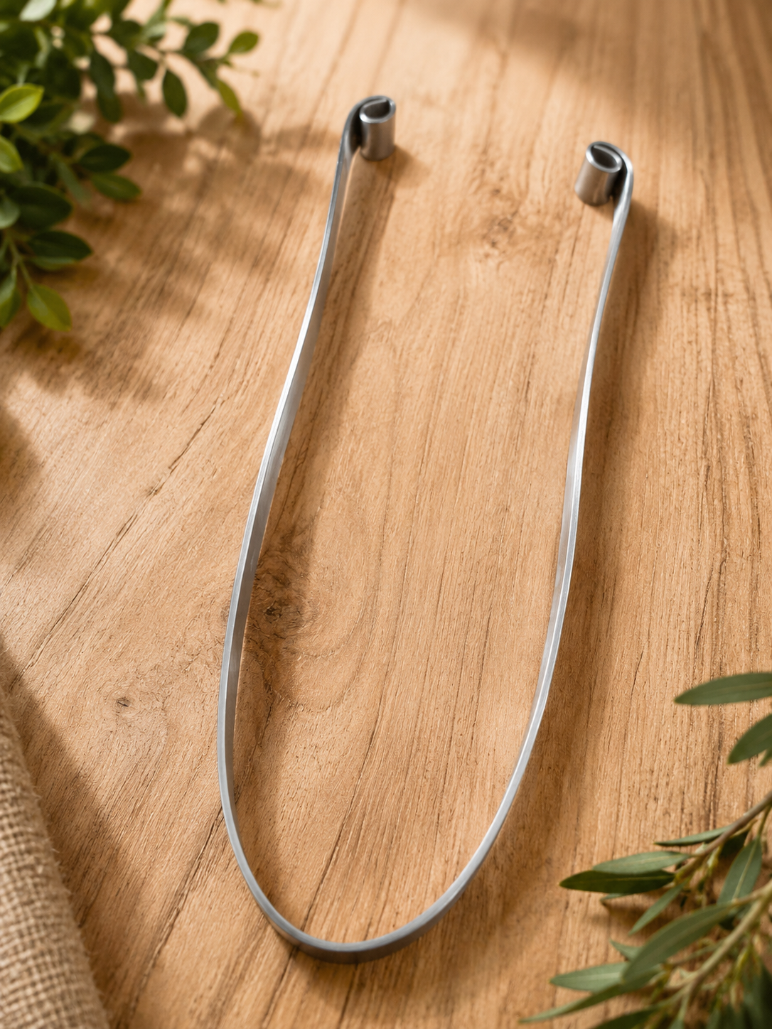 Lima de uñas metálica plateada en forma de U sobre una superficie de madera con ramitas de vegetación cerca.