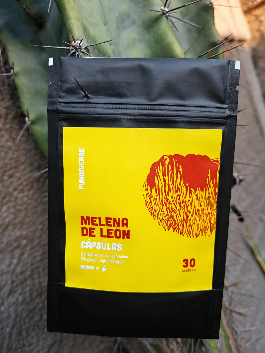 Bolsita de cápsulas MELENA DE LEÓN amarillas y negras sobre un fondo vegetal.