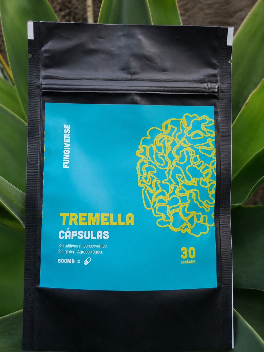Bolsita negra de cápsulas de Tremella con etiqueta turquesa y diseño amarillo, sostenida sobre hojas verdes.