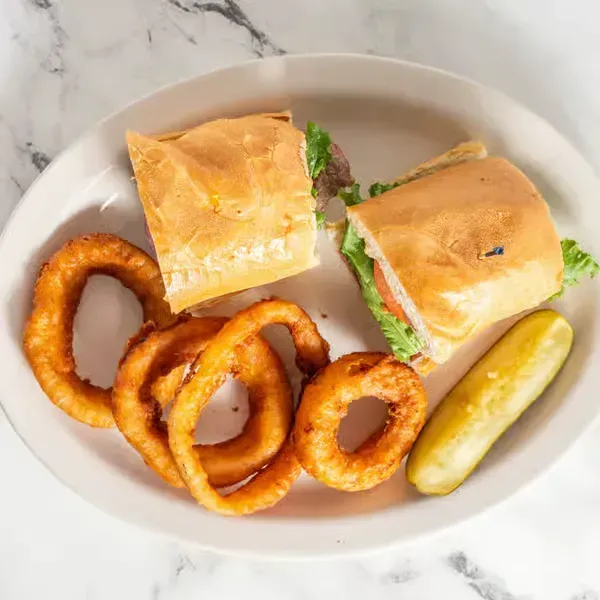 Plate with two sandwich halves, onion rings, and a pickle on a marble surface