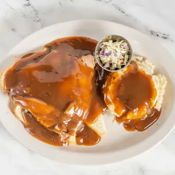 Plate of smothered fried pork chops with brown gravy, mashed potatoes, and coleslaw on a white plate
