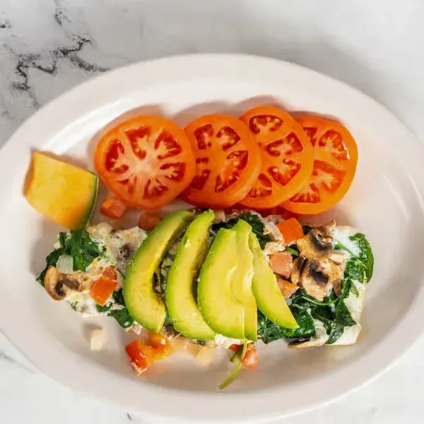 Plate with tomato slices, avocado, and a creamy vegetable salad on a white plate