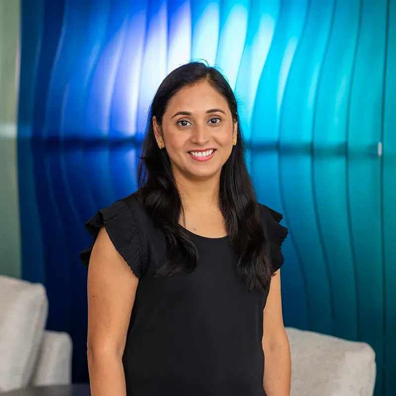 Woman smiling in a black top against a blue, curved wall background