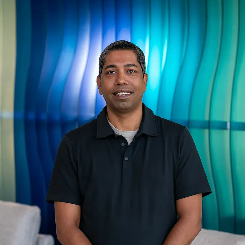 Smiling man in black polo standing before a blue and teal wavy wall