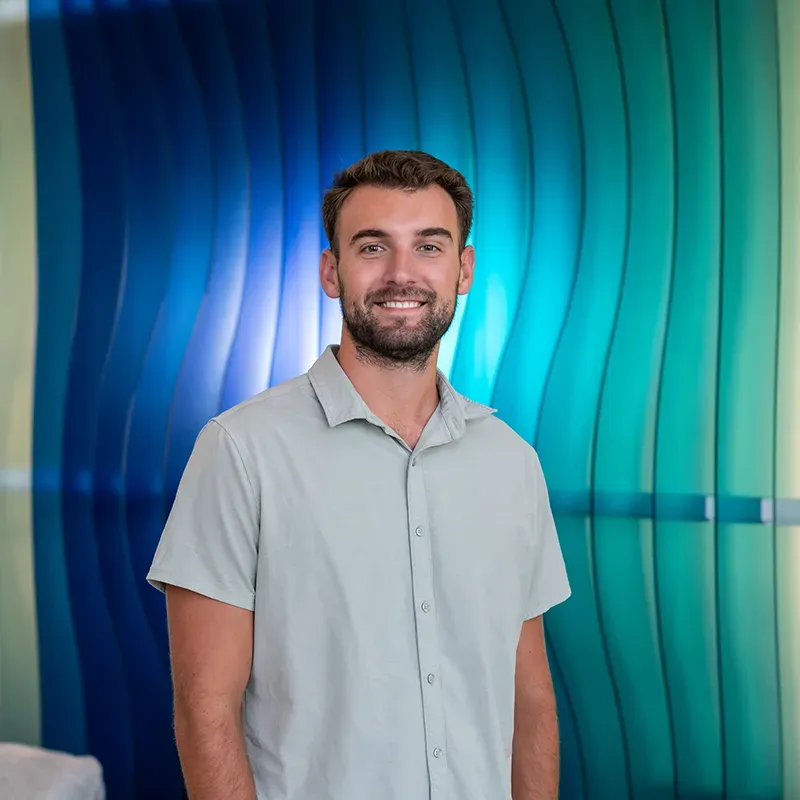 Smiling man standing before a blue-green wavy wall backdrop