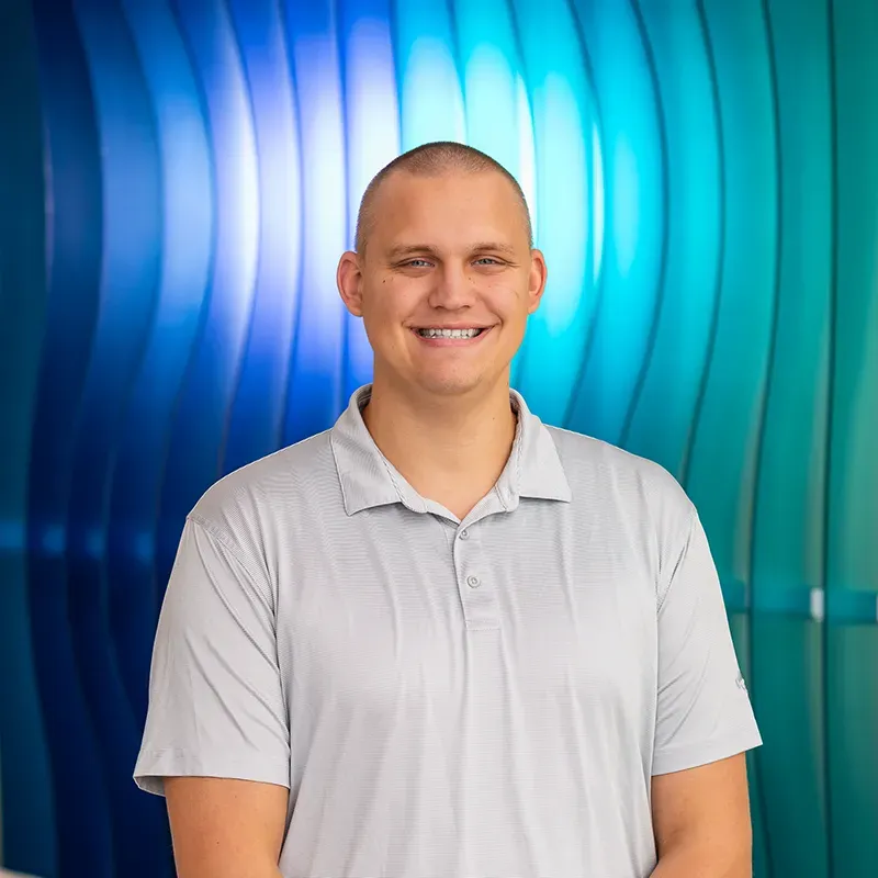 Smiling person in a light gray polo shirt standing before a blue and teal curved backdrop